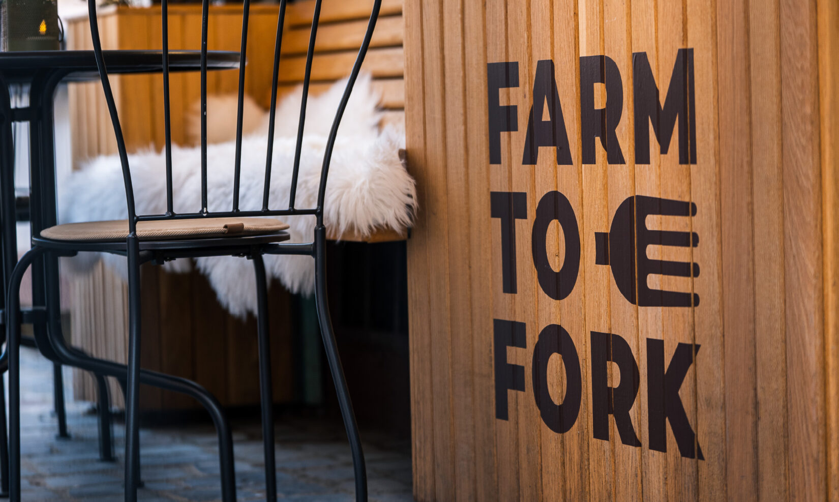 Jardinieră din lemn cu grafica Farm to Fork, lângă mesele de pe terasă