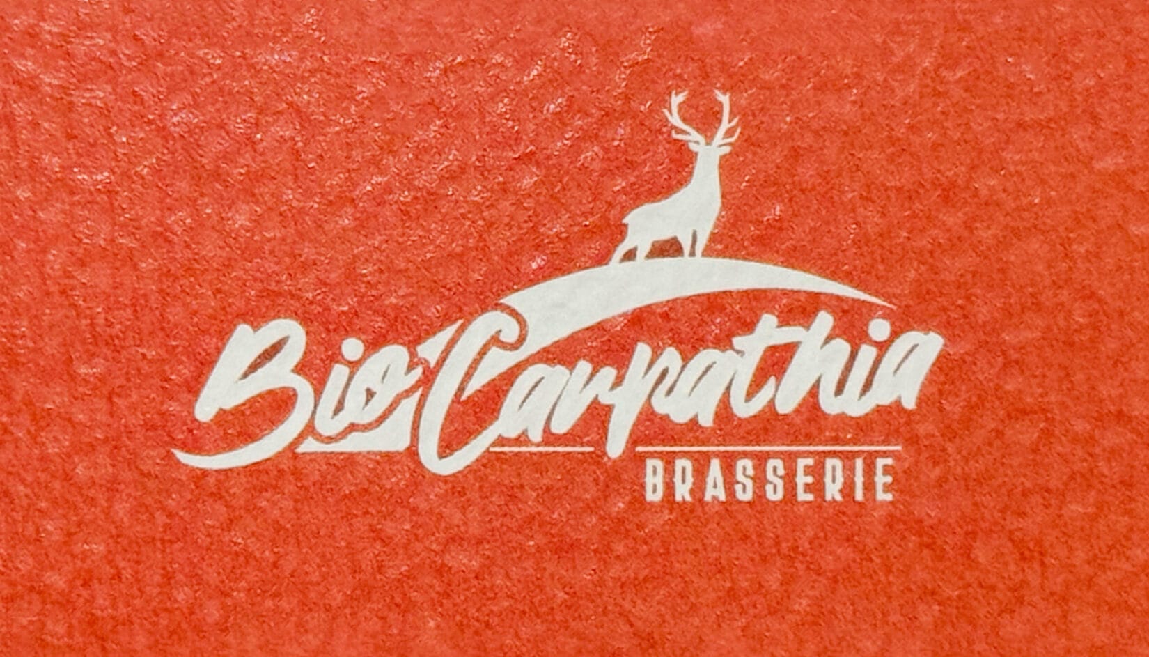 Logo-ul Brasserie Bio Carpathia în alb aplicat pe o suprafață texturată portocalie